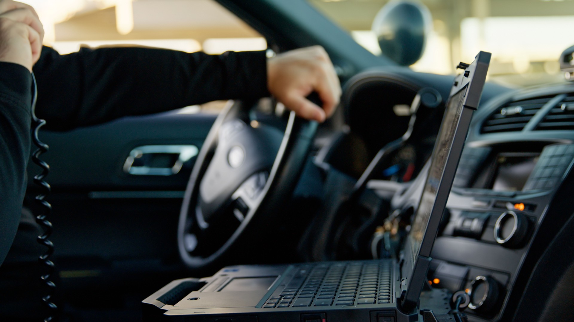 Police Officer Sitting in Parked Vehicle Using Laptop and Radio